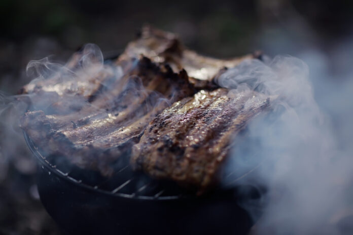 Costela sendo preparada no fogo de chão com fumaça ao redor.