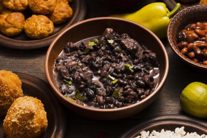 Feijoada gaúcha servida em tigela de cerâmica com acompanhamentos tradicionais ao redor.