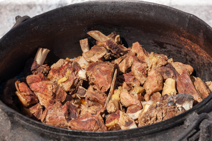 Carne de charque gaúcho sendo preparada em panela de ferro sobre fogo de chão.